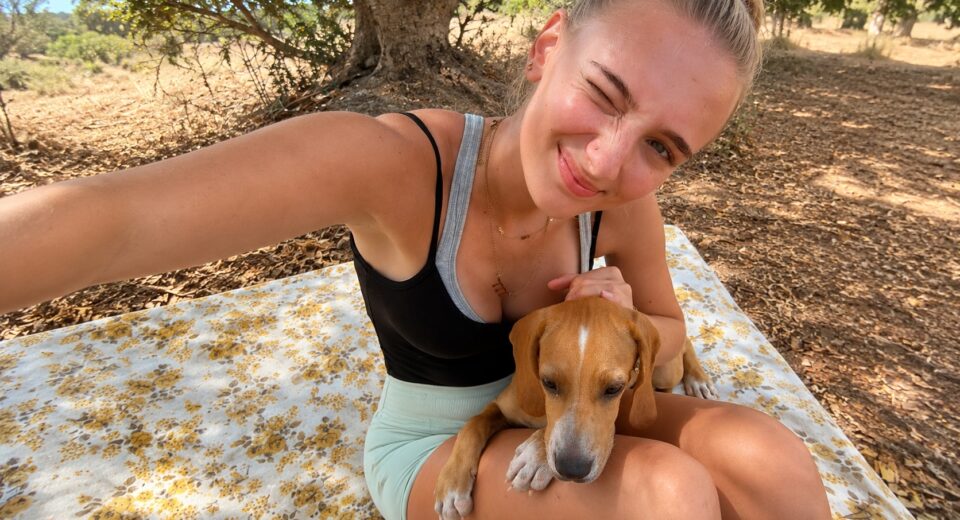 German student Luise sitting outdoors with Chilli Boy, a Maltese shelter dog adopted after her internship at the Association for Abandoned Animals.